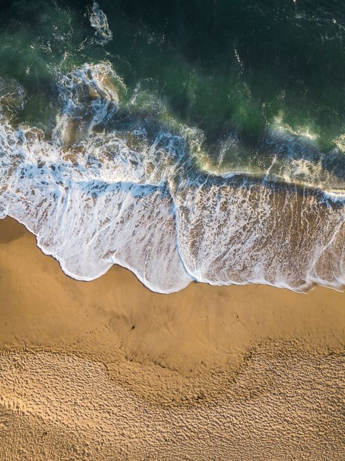Free A stunning aerial capture of waves crashing onto the sandy shore at Moss Beach, California. Stock Photo