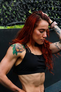 Portrait of a fit, tattooed woman in activewear with dyed hair, confidently posing outdoors.