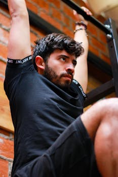 Man with a beard intensely focused while performing a pull-up in an indoor gym setting.