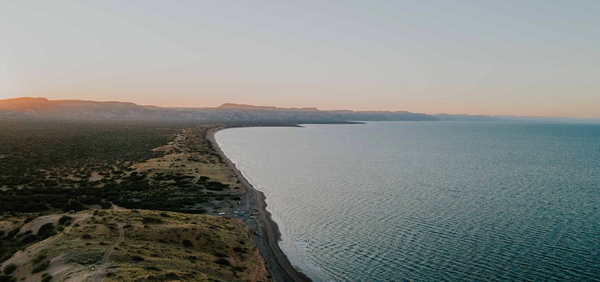 A breathtaking aerial view of a coastal landscape at sunset with rolling hills and a serene ocean.