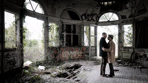 Двое мужчин, стоящих на коричневом полу внутри разрушенного здания