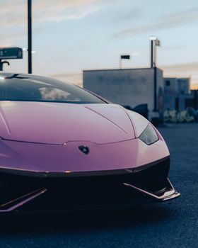 A sleek pink luxury car parked outdoors during sunset in a city environment.