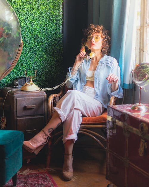 Young Woman Sitting on a Chair in a Corner of a Room and Talking on the Phone 