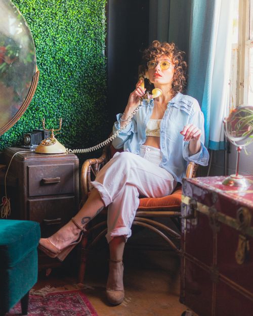 Free Young woman with curly hair talks on a vintage phone in a retro-themed room in Toronto. Stock Photo