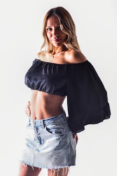 A fashionable woman poses confidently in a black top and denim skirt against a white background.