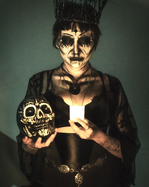 Free A dramatic Dia de Muertos portrait featuring a woman with a painted face holding a candle and skull. Stock Photo
