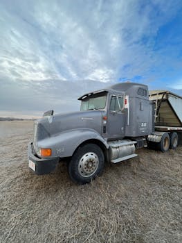 A robust semi-truck parked on a dry grass field beneath a vast blue sky, showcasing industrial strength and rural simplicity.