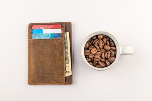 갈색 지갑 옆에 커피 콩이있는 흰색 머그잔