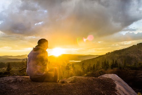 Free Person Sitting on Stone Facing Sunset Stock Photo