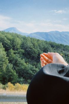 A person reaching out towards green mountains on a sunny day, evoking peace and connection with nature.