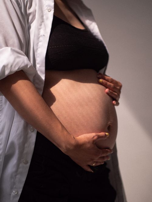 Free Close-up of a pregnant woman gently cradling her belly in soft, natural light. Stock Photo