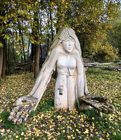 Free Wooden sculpture of a female figure with outstretched arms in an autumn park. Stock Photo