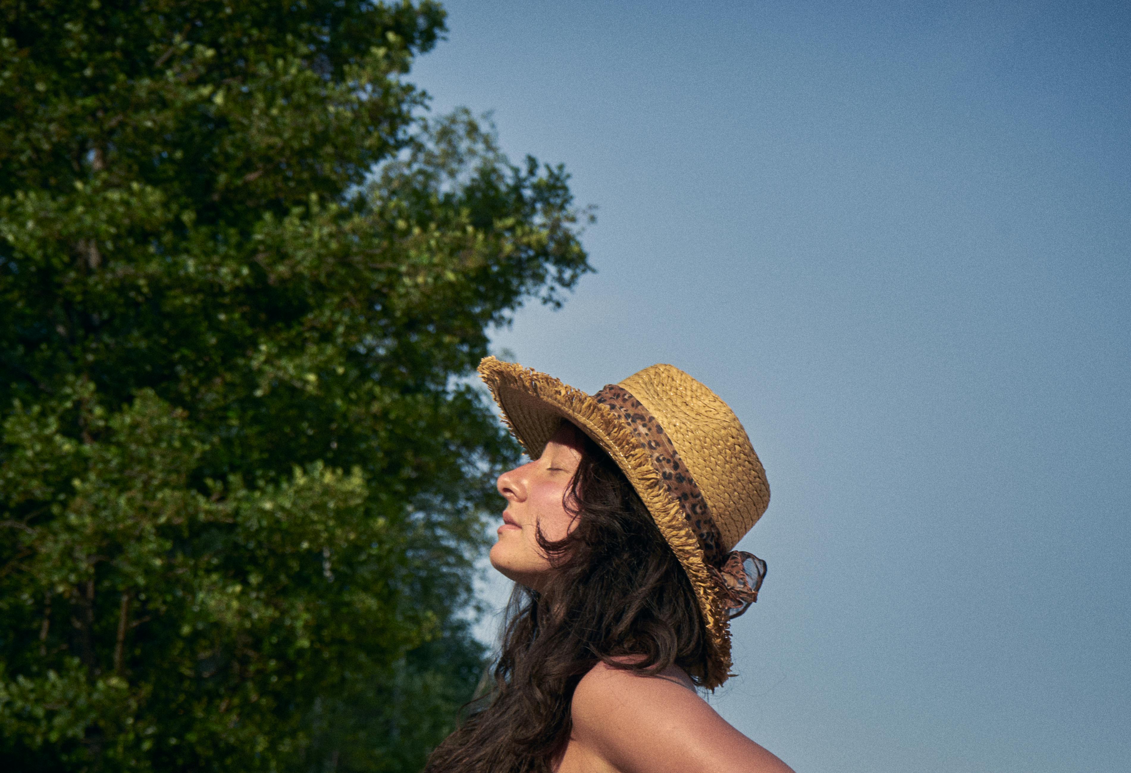 Portrait of a woman in a straw hat relaxing outdoors with eyes closed, embracing tranquility.