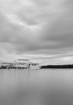 A tranquil black and white photo of a harbor with a boat under cloudy skies. Perfect for travel and nautical themes.