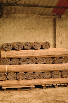 Neatly stacked bamboo rolls in a rustic warehouse, showcasing natural materials for construction or crafts.