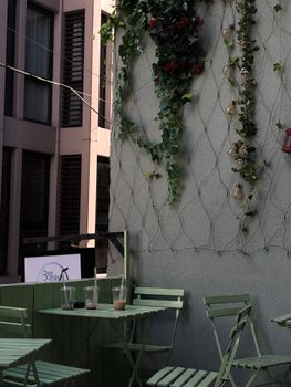Charming outdoor cafe corner with a wooden table, folding chairs, and green creeper plants on a wall.