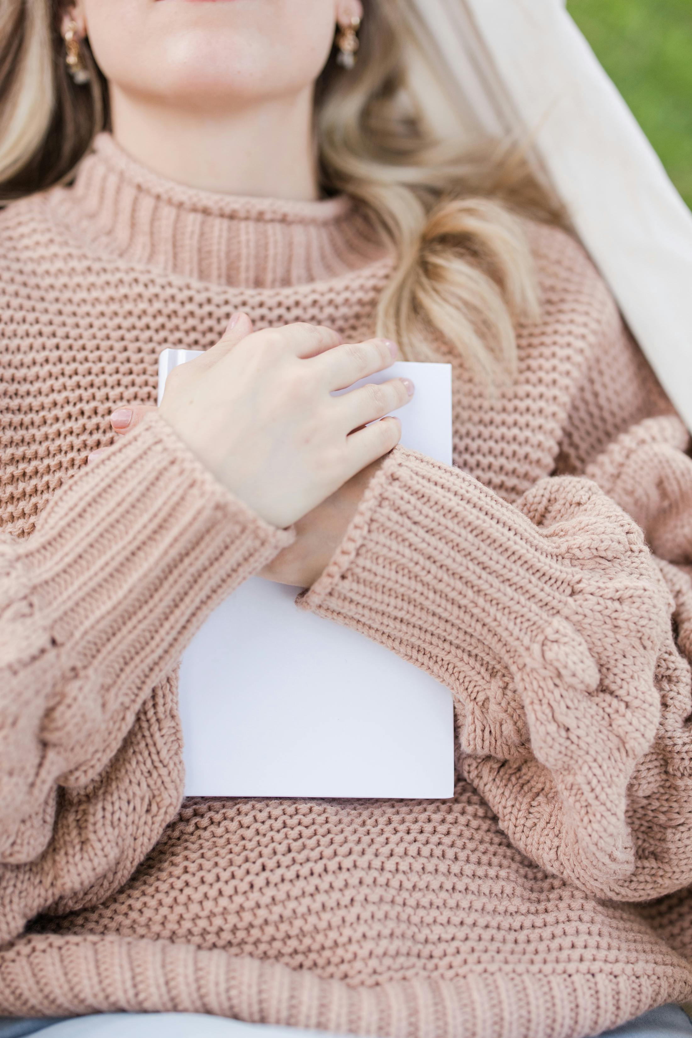 Woman in a knitted sweater holding a blank notebook outdoors. Serene and cozy vibe.