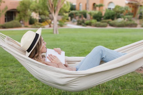 Woman Wearing a Summer Hat Relaxing with a Book on a Hammock