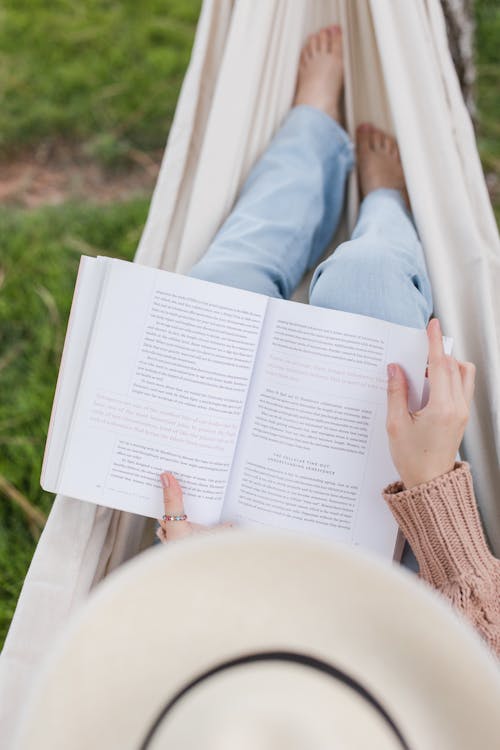 Free Top View of a Woman Wearing a Hat Reading a Book in a Hammock Stock Photo