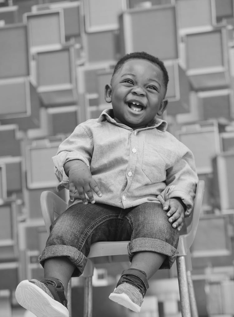 Grayscale Photo Of A Happy Little Boy Sitting In An Armchair