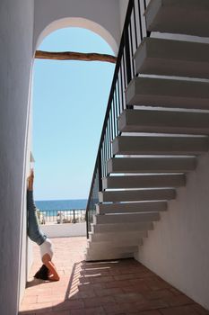 Woman practicing yoga headstand near stairs with ocean view, showcasing flexibility and balance.