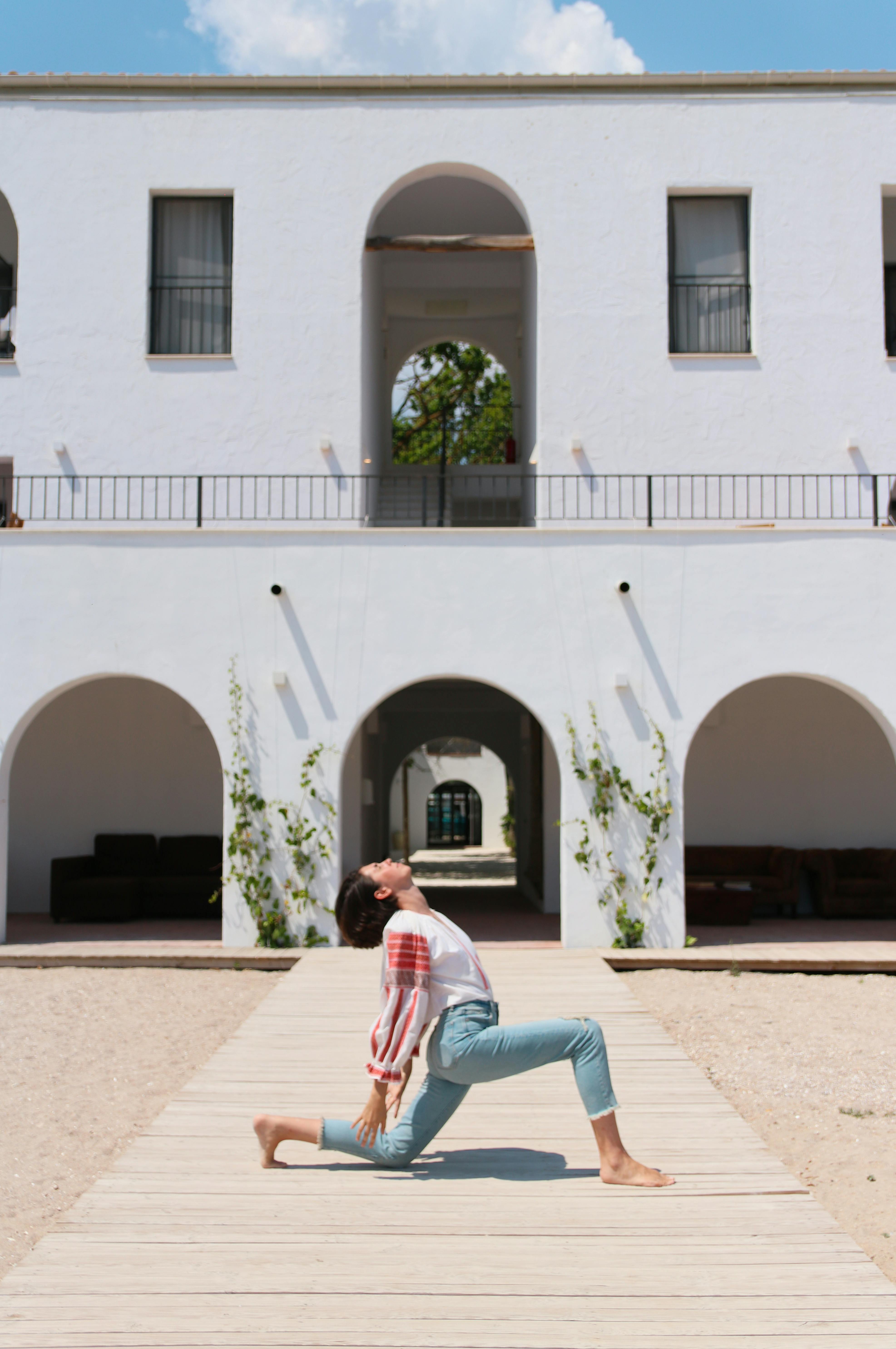 Woman performing a yoga pose in front of a modern white building on a sunny day.