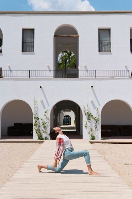 Woman performing a yoga pose in front of a modern white building on a sunny day.