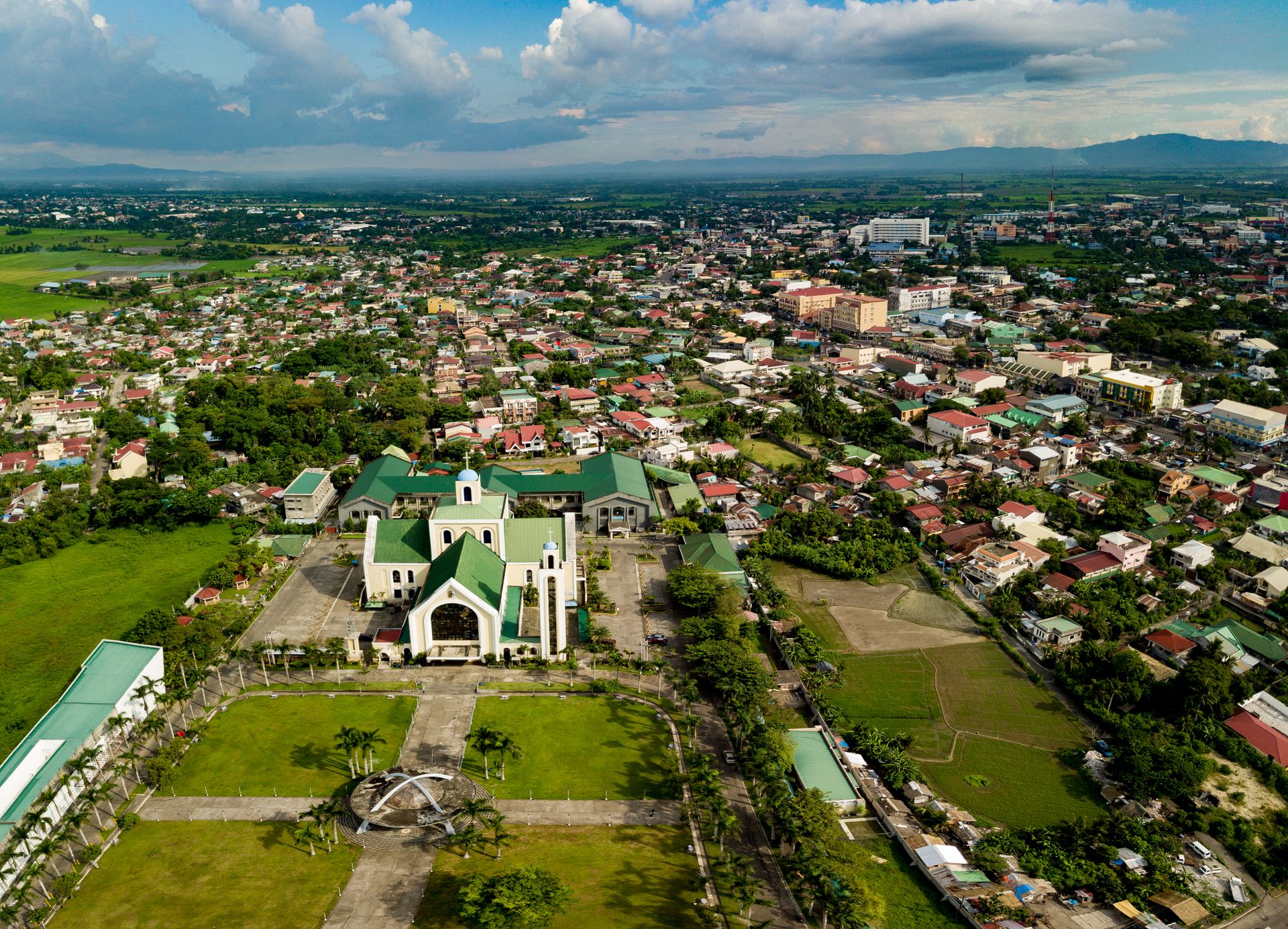 A panoramic aerial shot capturing a cityscape with a prominent green-roofed church surrounded by lush greenery.