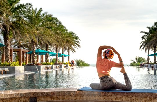 Woman practicing yoga by a luxurious poolside in a tropical resort, highlighting relaxation and wellness.