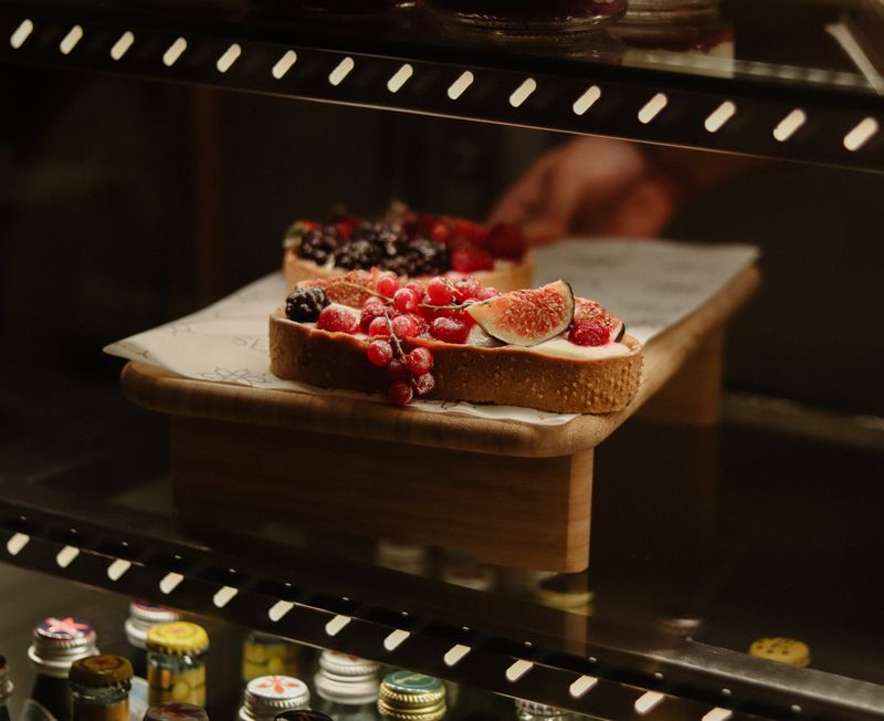 Delicious artisan bread topped with fresh figs, raspberries, and currants in a cafe display.