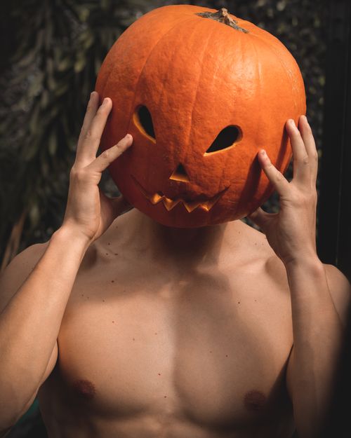 Free A topless man holds a carved pumpkin on his head, celebrating Halloween outdoors. Stock Photo