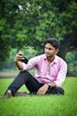 Man Sitting on the Grass in a Park and Taking a Selfie