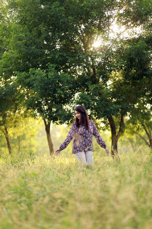 Free Fashionable woman walking through a sunlit park with lush green trees in the background. Stock Photo