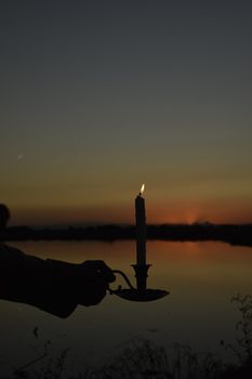 A tranquil evening scene with a candle's silhouette against a sunset lake.