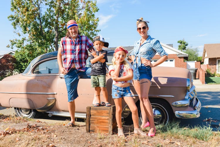 Family Posing By A Vintage Car In Sunlight