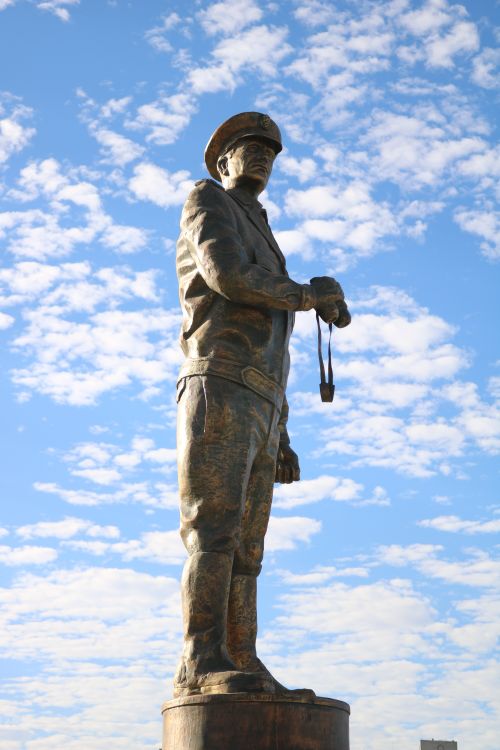 Free A striking bronze statue of a soldier set against a vibrant blue sky with scattered clouds. Stock Photo