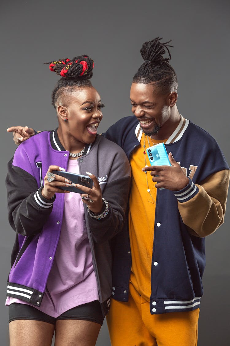 A Man And Woman Having Fun While Holding Their Mobile Phones