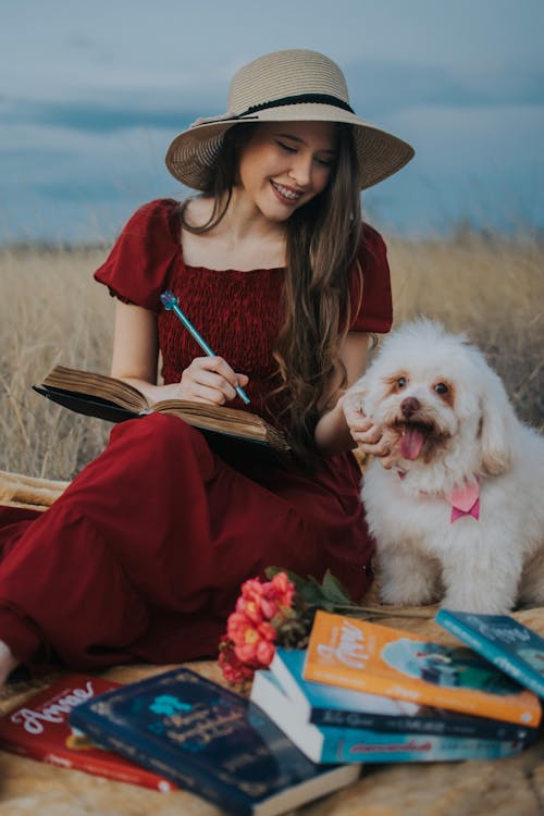 Smiling Woman in Red Dress and Hat Sitting with Dog on Picnic