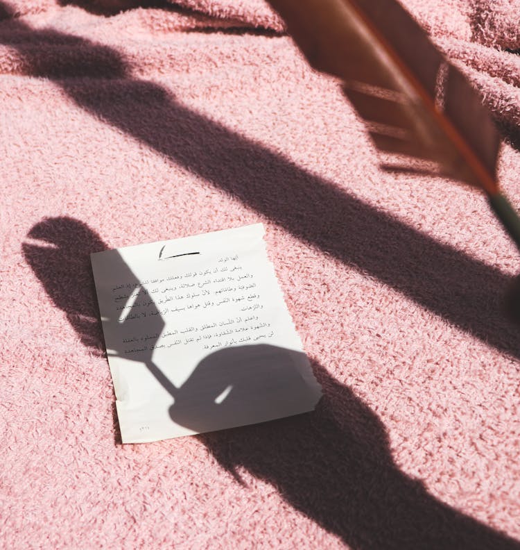 Shadow Of Hand Holding Feather Above Piece Of Paper