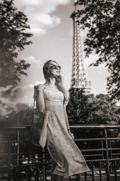 Grayscale Photo of a Woman Standing near the Eiffel Tower