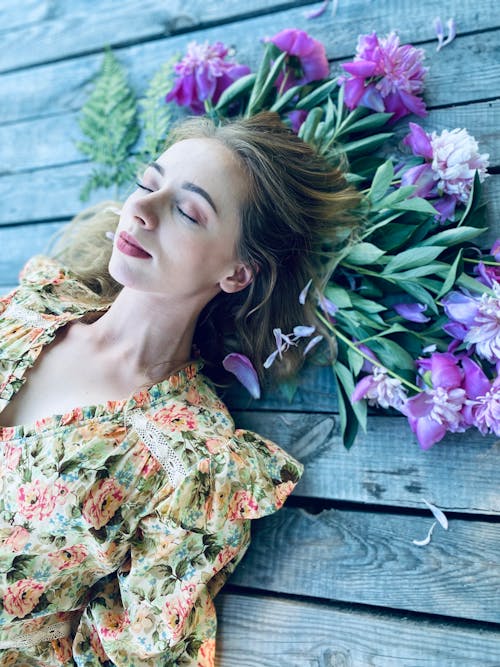 A Woman in Floral Dress Lying on the Wooden Floor and Flowers