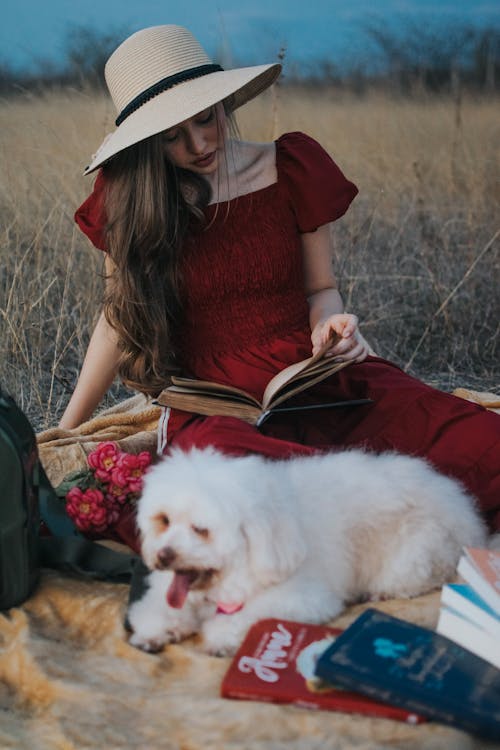 Woman in a Red Dress Reading a Book while Sitting beside a Dog