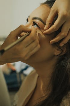 A young woman getting eye makeup applied by an artist.