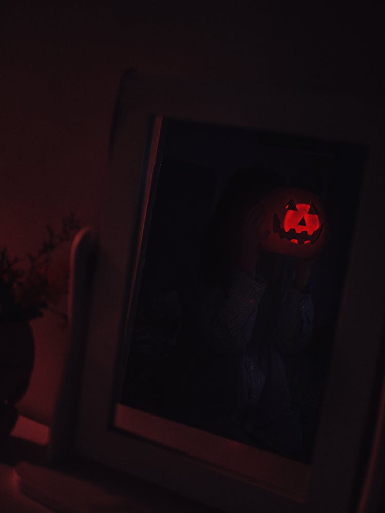 Person Holding Carved Pumpkin Reflecting In Mirror