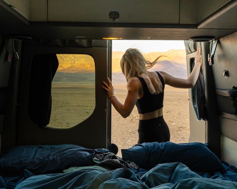 A woman steps out of a camper van into the desert landscape of Death Valley at dawn, ready for an adventure.