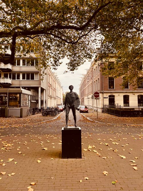 Free Statue in a leafy Amsterdam street during fall season, capturing city charm. Stock Photo