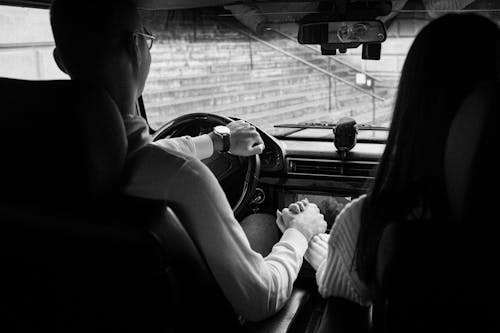 A Grayscale of a Couple Holding Hands in the Car