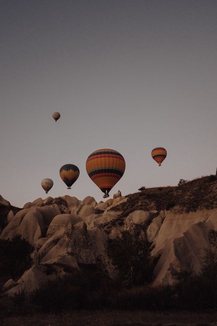 Colorful hot air balloons soar over unique rock formations in Cappadocia, Turkey, creating a breathtaking view.