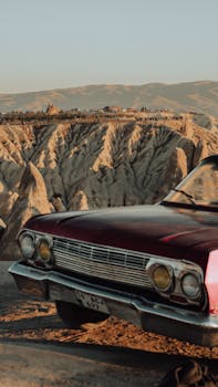 Classic vintage car parked by a stunning canyon landscape during sunset, capturing nostalgic travel vibes.