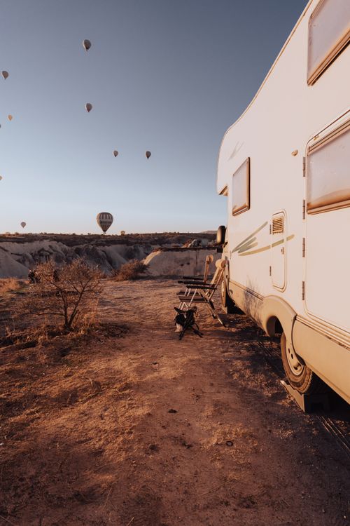 Free A serene camping scene in Göreme, Turkey, with hot air balloons rising over a rugged landscape. Stock Photo